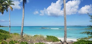 A beach with clear turquoise water, palm trees, and a distant rocky outcrop. - Lil Cay Villa, with a Newly Renovated Kitchen (Steventon)