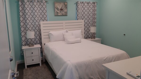 A bedroom with a bed, two bedside tables, a nightstand, a lamp, and a wall-mounted artwork.