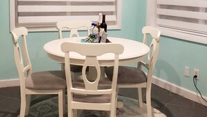 Un'area pranzo con un tavolo rotondo e quattro sedie, due finestre con persiane e un lampadario.