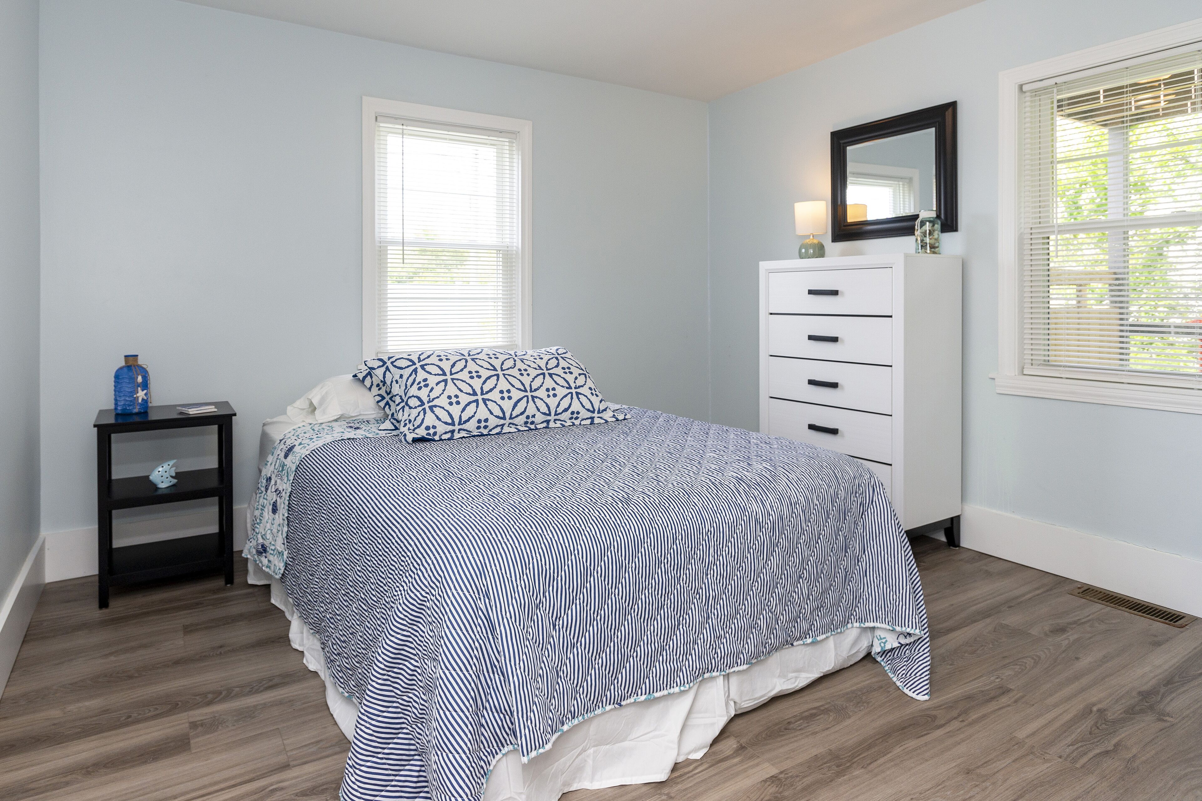 A bedroom with a bed, a dresser, a nightstand, and a window with blinds.