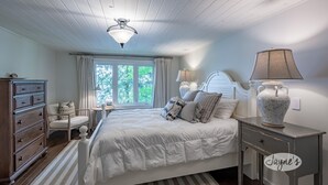 Quarto com uma cama grande, cômoda, mesa de cabeceira, abajur e janela com cortinas.