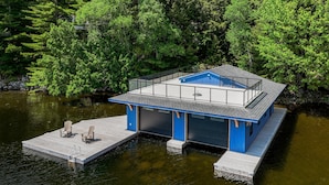 Uma casa flutuante moderna com esquema de cores azul e branco, atracada em águas calmas, rodeada por vegetação exuberante.