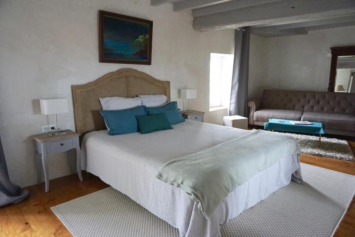 A bedroom with a large bed, two bedside tables, a nightstand, a sofa, and a painting on the wall.