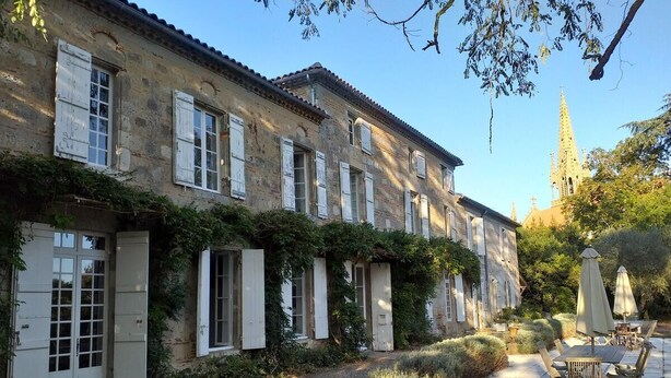 A courtyard with a stone floor, outdoor seating, and a building with shutters and vines. - Ecrin des sens - Manoir en Agenais (Puch-d'Agenais)