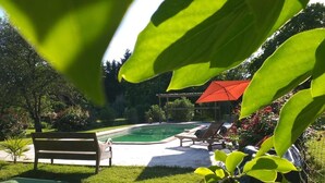 A swimming pool with a wooden bench and lounge chairs, surrounded by greenery and a red-roofed structure. - Ecrin des sens - Manoir en Agenais (Puch-d'Agenais)