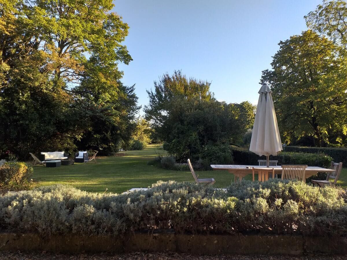 A garden with a wooden table and chairs, surrounded by lush greenery and trees.