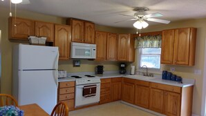 A kitchen with wooden cabinets, a microwave, a refrigerator, a stove, and a ceiling fan. - The Lake House at Turtle Cove: Cozy relaxing lake home with dock on wooded lot. (Eutawville)