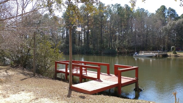 A wooden dock extending into a calm lake surrounded by trees. - The Lake House at Turtle Cove: Cozy relaxing lake home with dock on wooded lot. (Eutawville)