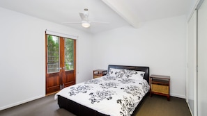 Een slaapkamer met een bed, een plafondventilator, een nachtkastje en een raam met uitzicht.