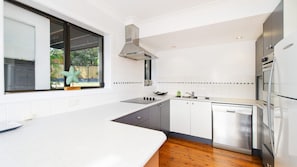 A modern kitchen with white cabinetry, a stainless steel range hood, a dishwasher, and a window with a starfish decoration.