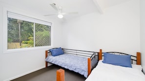A single bed with a headboard, a window with a view of greenery, and a ceiling fan.