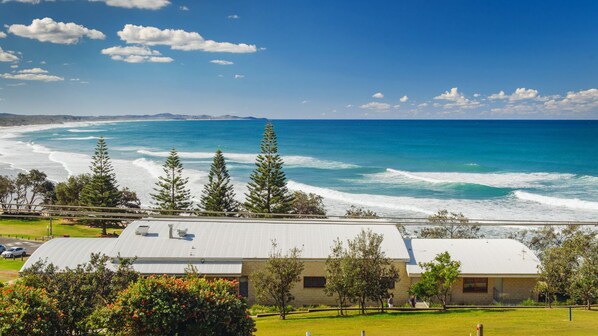 A coastal building with a flat roof, surrounded by greenery and a view of the ocean.
