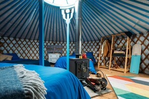 A cozy yurt interior with a bed, a small stove, and a wooden shelf with boots.