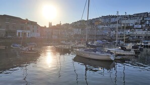 A marina with boats docked, buildings in the background, and the sun reflecting on the water.