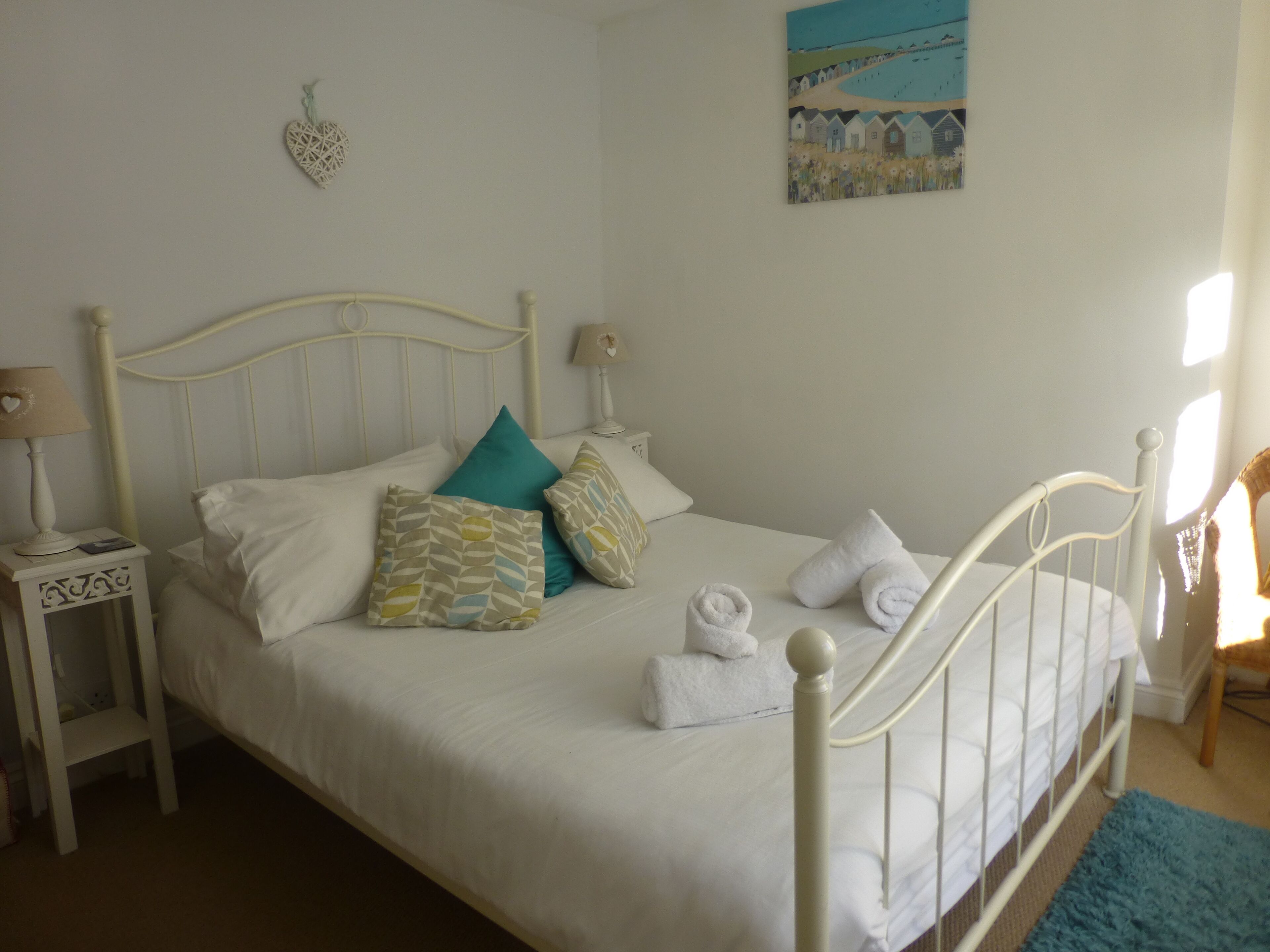 A neatly made bed with white linens and decorative pillows, a bedside table with a lamp, and a painting on the wall.