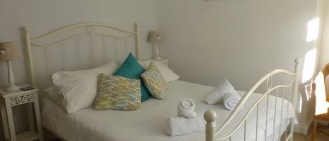 A neatly made bed with white linens and decorative pillows, a bedside table with a lamp, and a painting on the wall.