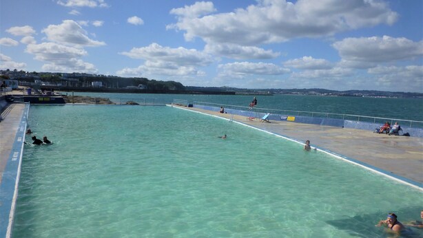 A swimming pool with clear water, a lifeguard chair, and a few people swimming.