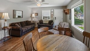 A living room with a brown leather sofa, a patterned armchair, a wooden dining table, and a ceiling fan. - Lake Street 425 ~ Fantastic 2bed/2bath Home Right (Sandpoint)