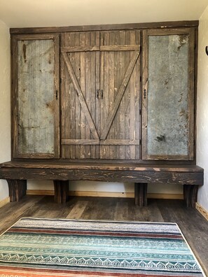 A rustic wooden bench with a decorative backrest and a patterned rug on the floor.