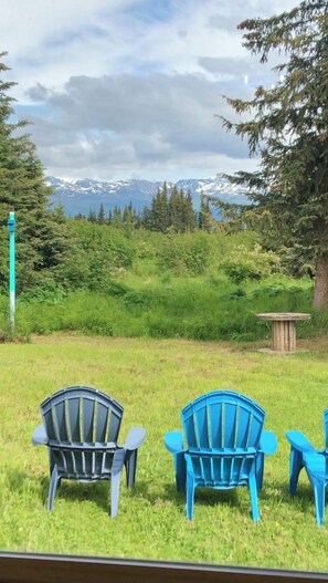 Relax in a serene outdoor space with Adirondack chairs overlooking a lush green field and distant mountains.