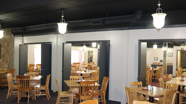 A dining area with wooden tables and chairs, a stone wall, and hanging light fixtures. - Friendship Inn (Altus)