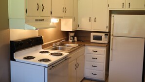 A kitchen with white cabinets, a stove, a sink, a microwave, and a refrigerator. - Friendship Inn (Altus)