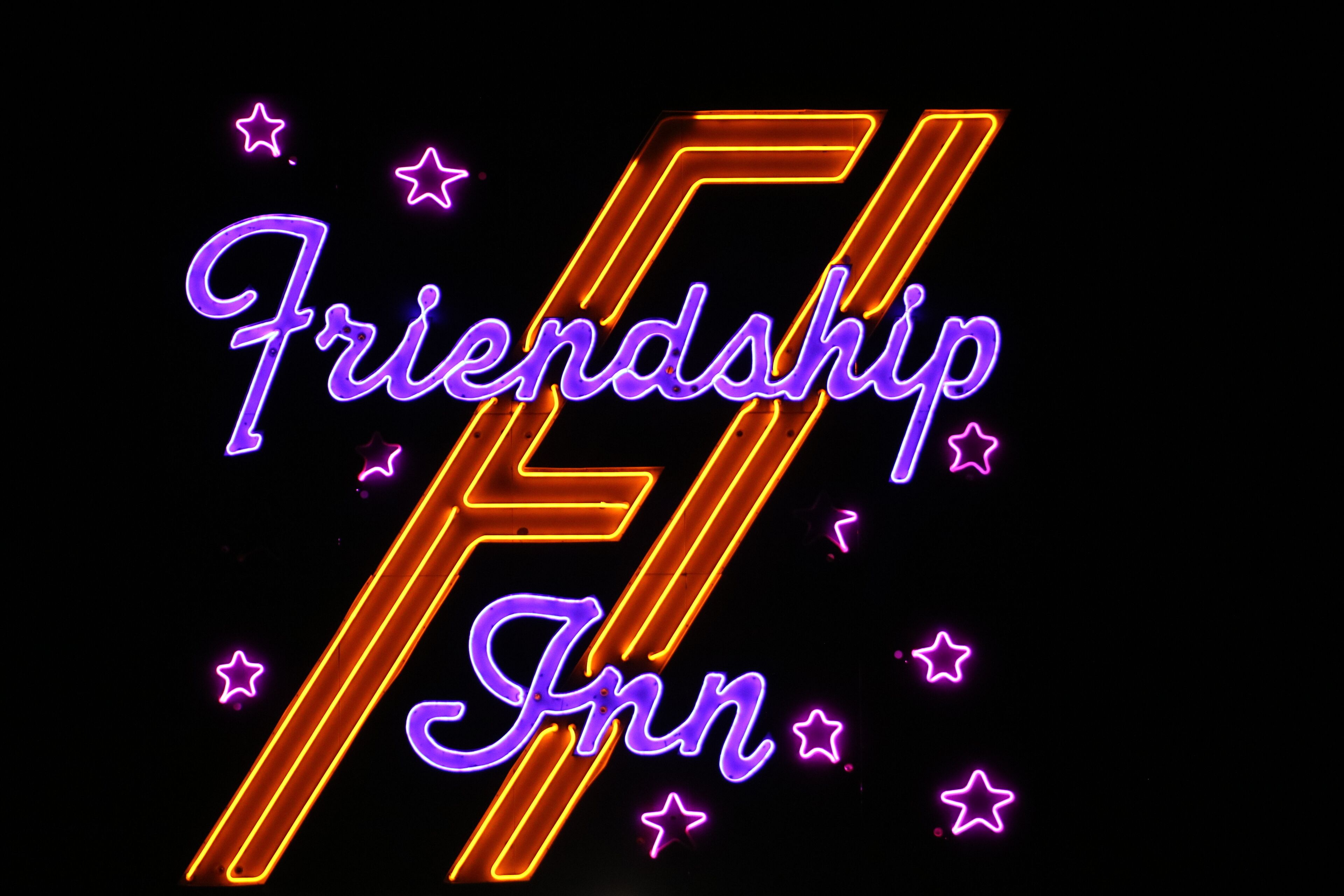 Ein Neon-Schild mit der Aufschrift 'Friendship Inn' und einem stilisierten 'F' in Orange und Lila.