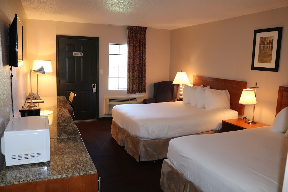 A hotel room with two beds, a desk with a microwave, a TV, and a window with curtains.
