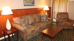 A living room with a brown leather sofa, two matching armchairs, a wooden coffee table, and two lamps on side tables. - Friendship Inn (Altus)