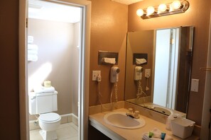 A bathroom with a toilet, sink, and mirror. There are lights above the mirror and a hairdryer on the wall.