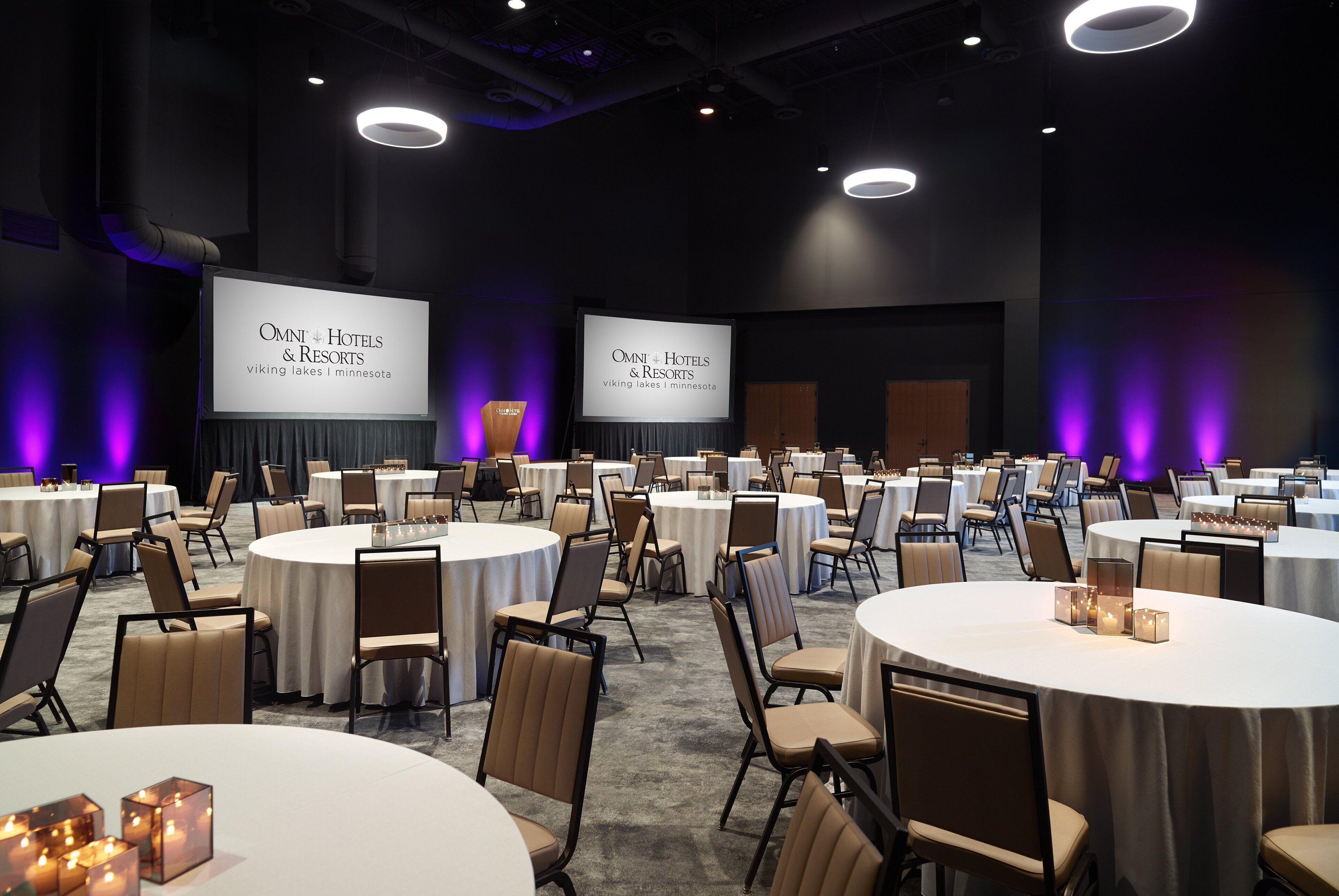 A conference room with round tables, chairs, and a large screen displaying "OMNI Hotels & Resorts viking lakes i Minnesota".