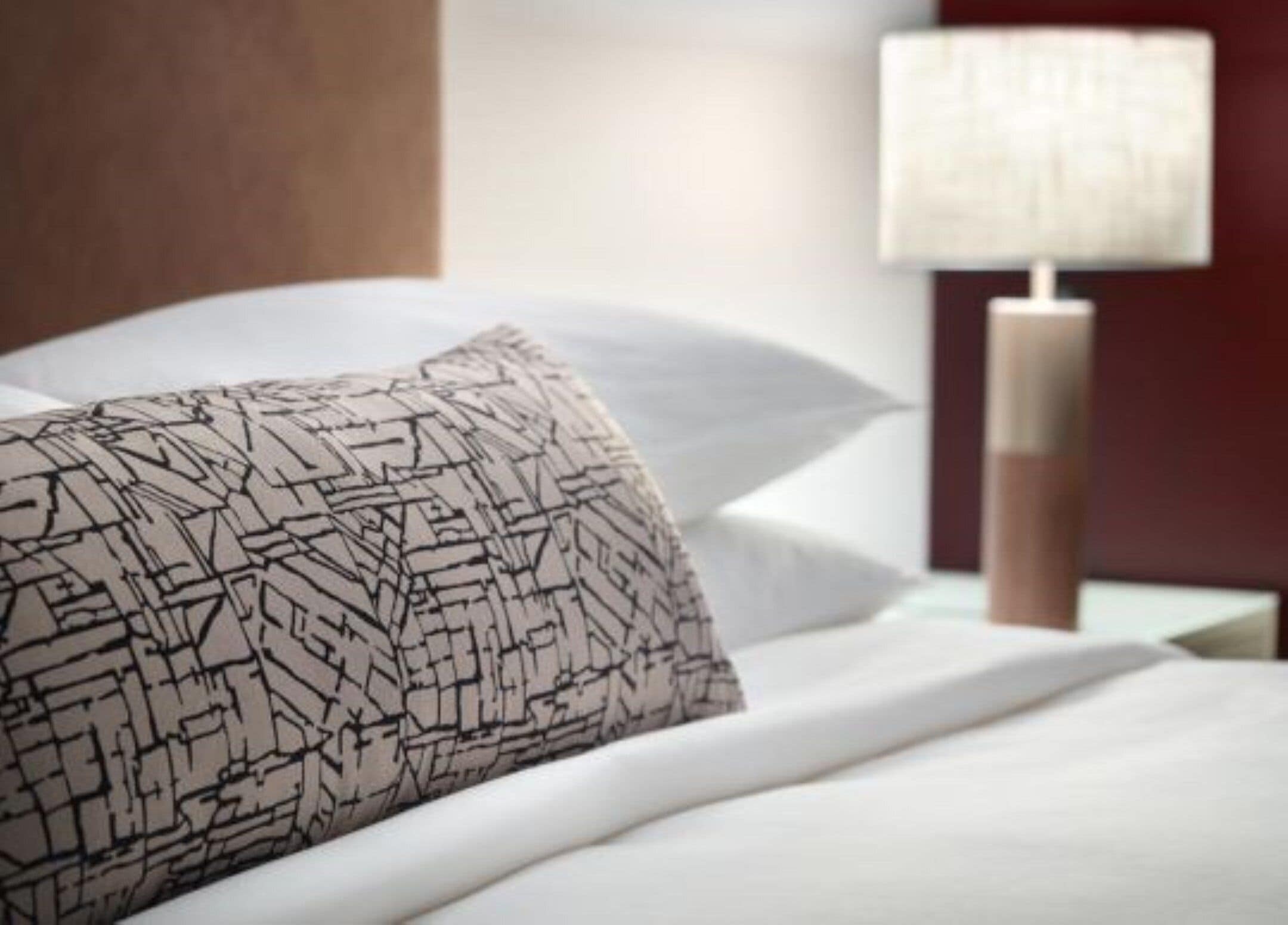 A neatly made bed with a patterned pillow, a bedside lamp, and a wooden headboard.