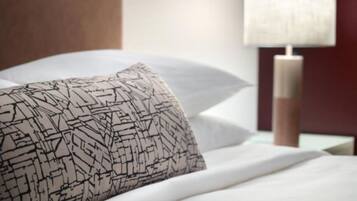 Una cama bien hecha con un cojín estampado, una lámpara de noche y un cabecero de madera.