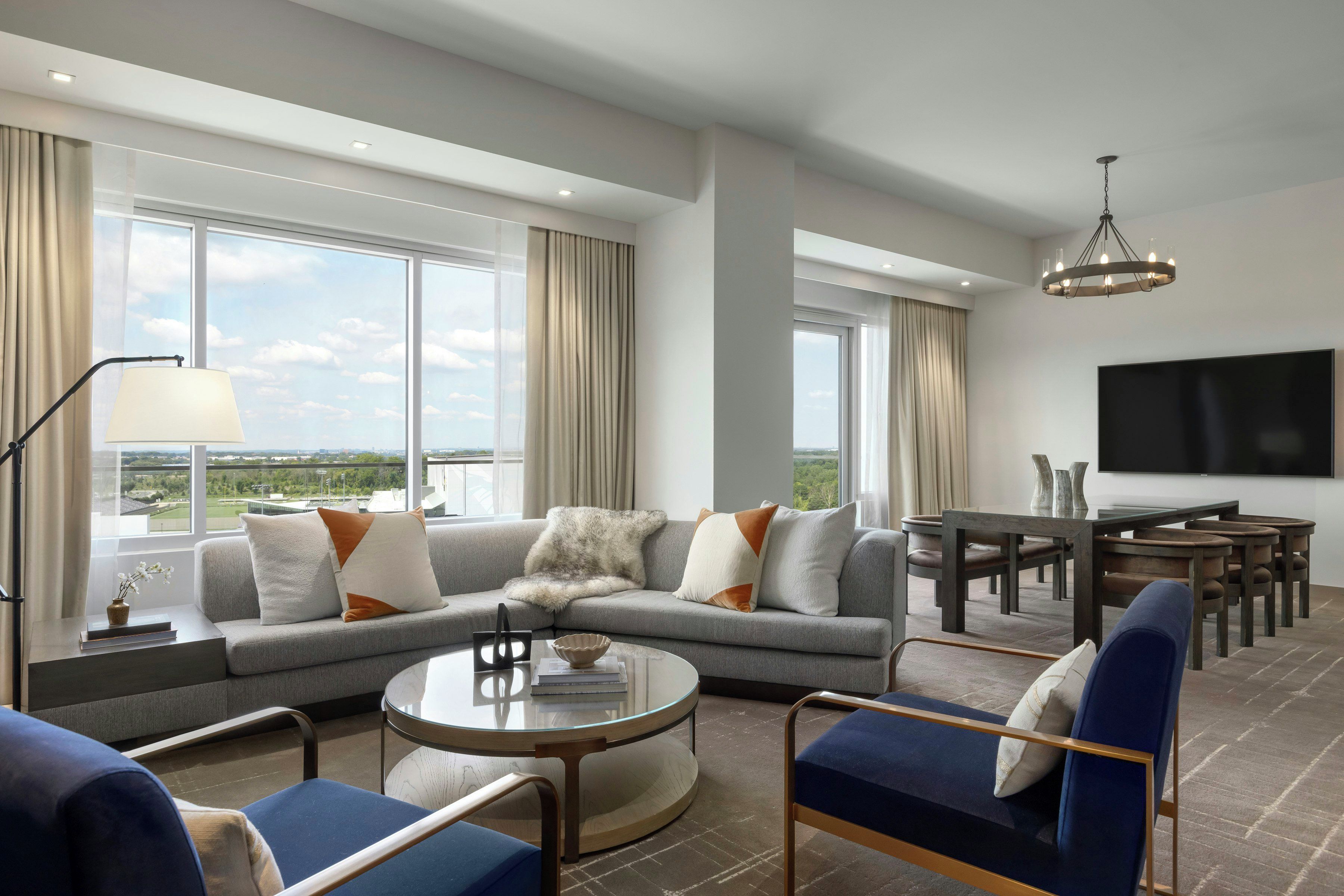 A modern living room with a sectional sofa, a round coffee table, and a dining area with a TV mounted on the wall.