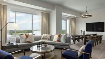 A modern living room with a sectional sofa, a round coffee table, and a dining area with a TV mounted on the wall.