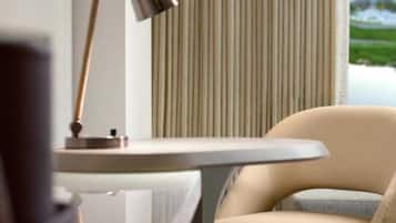 A modern room with a round table, a chair, a lamp, and a window with vertical blinds.