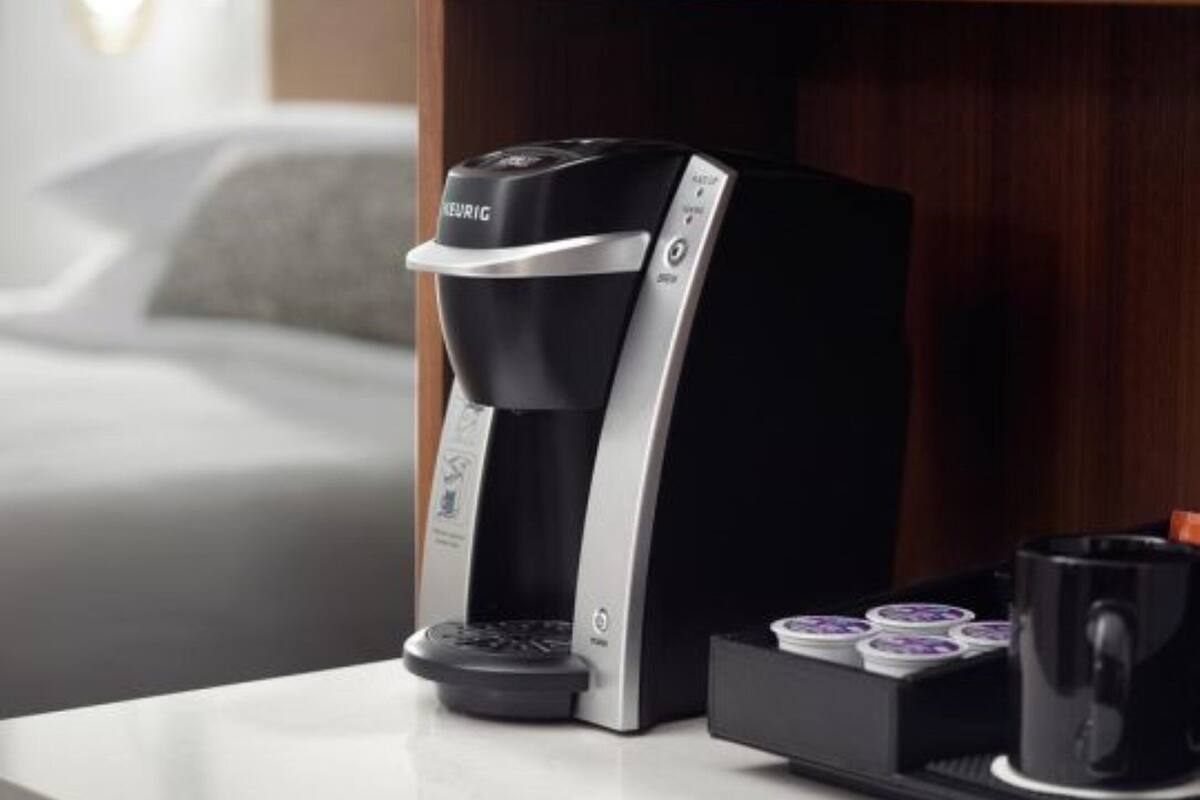 Una cafetera Keurig sobre una mesa con una bandeja de cápsulas de café y una taza.