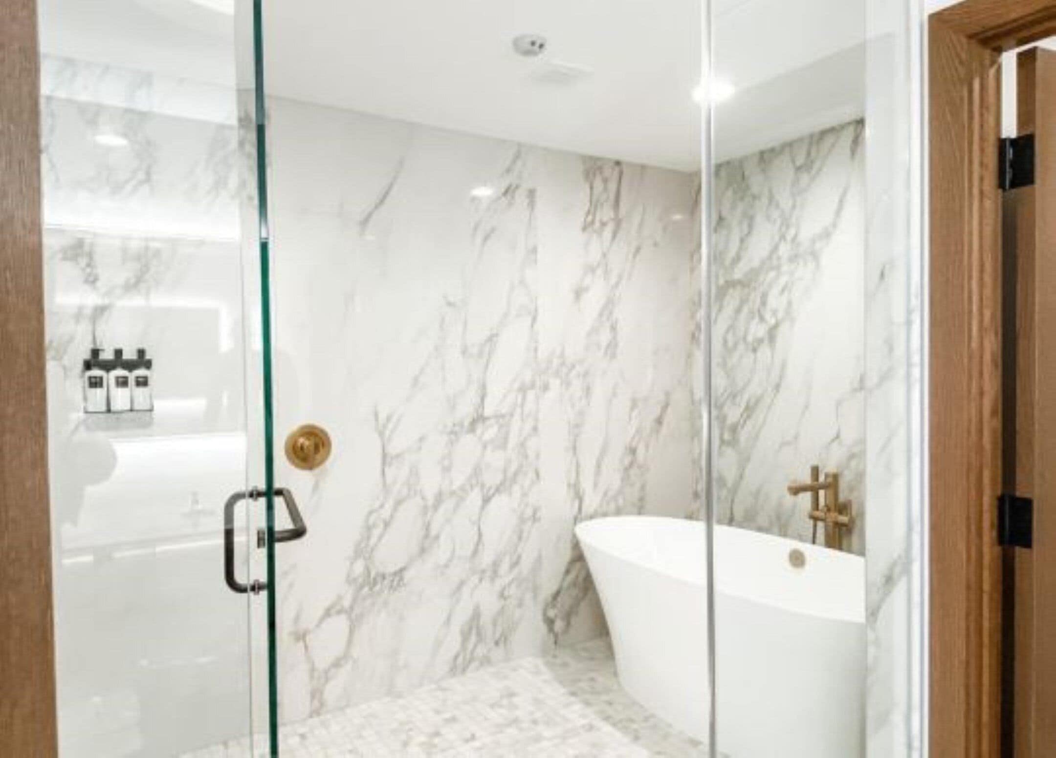 Een moderne badkamer met een douchecabine van glas, een vrijstaand bad en marmeren wanden.