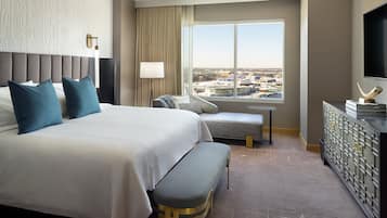 A hotel room with a large bed, a bench, a desk, a TV, and a view of the city.