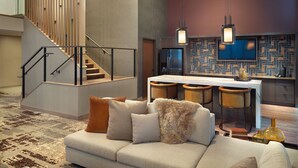 Una sala de estar moderna con un sofá, una escalera y una cocina con salpicadero de baldosas tipo espiga e iluminación colgante.