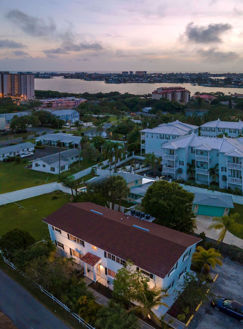 An aerial view of a residential area with houses, a large body of water, and distant buildings.