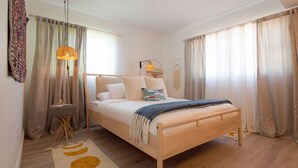 A bedroom with a wooden bed, a bedside lamp, a small table, and a patterned rug. - Stylish & Eclectic Modern 2/2 Apt - WeArePeaceful (South Pasadena)