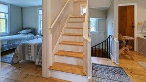 A bedroom with a bed, a window, and a staircase leading to another room. - 1810 Brook Side Mill/House / EV Level 2 Charging on Site (Shelburne Falls)