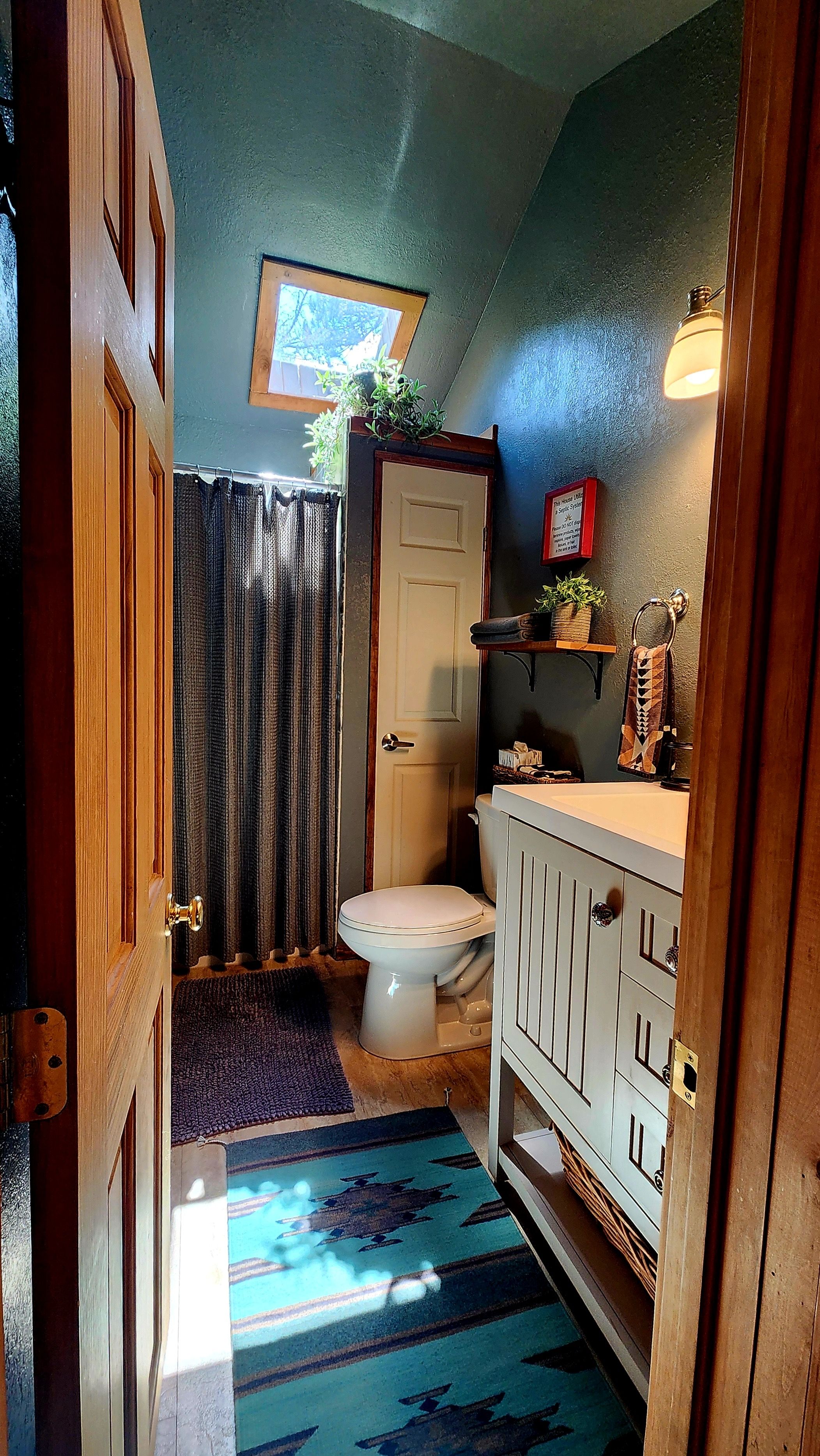 A bathroom with a toilet, a sink, a shower curtain, a towel rack, and a small window.