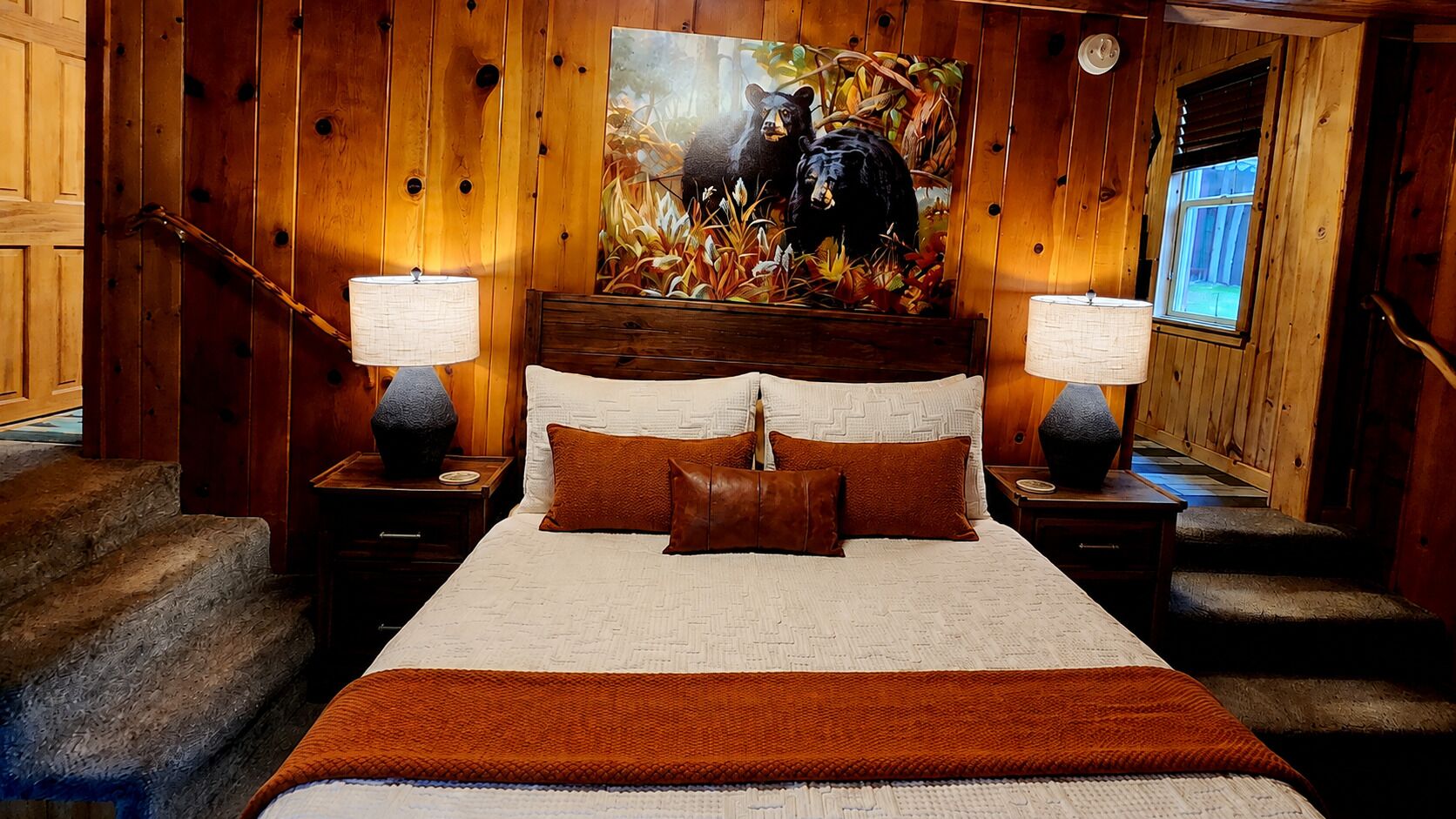 A wooden-paneled bedroom with a large bed, two nightstands, a painting of a bear, and a window.