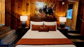 A wooden-paneled bedroom with a large bed, two nightstands, a painting of a bear, and a window.