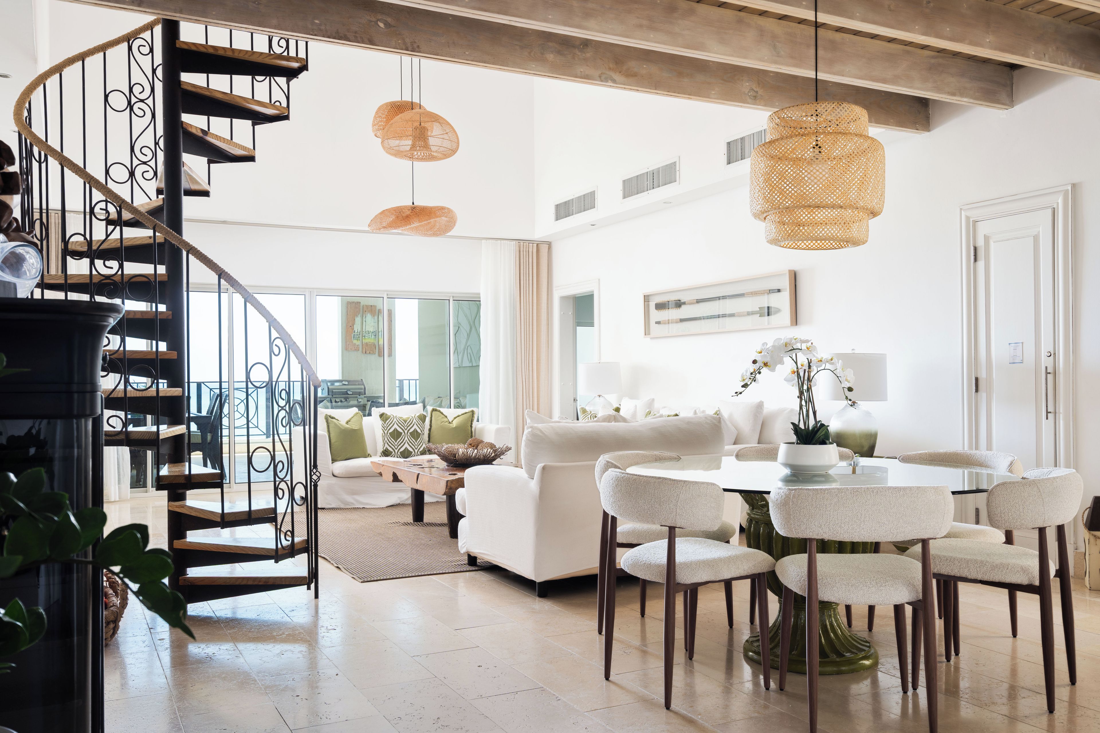 Un intérieur moderne avec un escalier en colimaçon, un coin repas doté de tables rondes et un salon avec un canapé et des coussins décoratifs.
