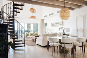 Een modern interieur met een wenteltrap, een eethoek met ronde tafels, en een woonkamer met een bank en decoratieve kussens.