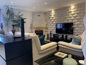 Een moderne woonkamer met een stenen openhaard, een flatscreen televisie aan de muur en een comfortabele zithoek met witte banken en een salontafel.