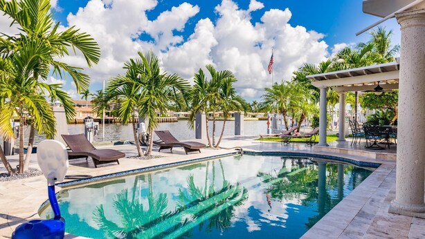 Ein Swimmingpool mit Liegestühlen und Palmen, umgeben von einer überdachten Terrasse.
